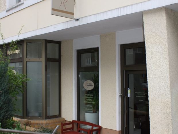 Eingang der Praxis an der Vinetastraße mit Praxisschild und roter Bank